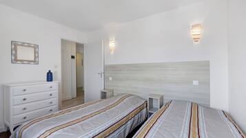 Une chambre avec deux lits, une commode, un miroir et deux lampes fixées au mur.
