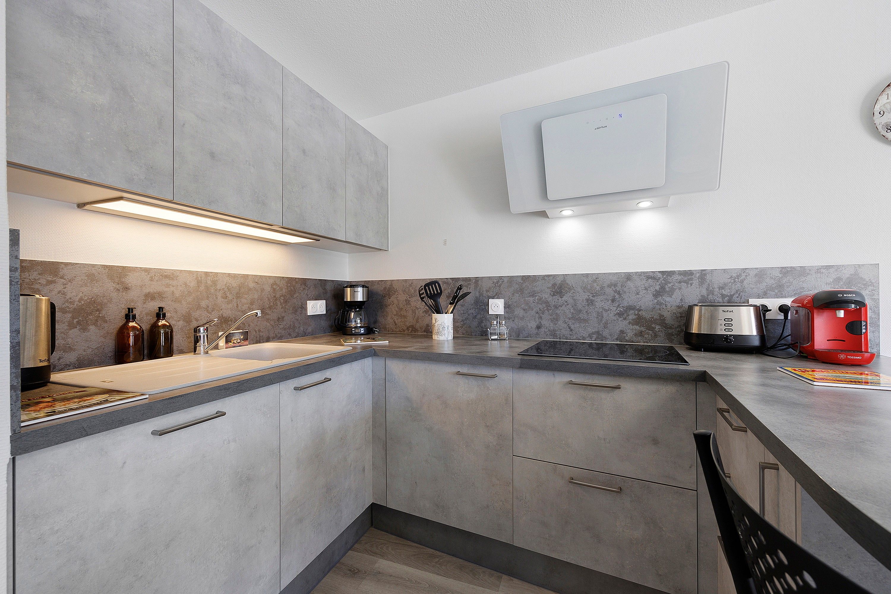A modern kitchen with grey cabinetry, a built-in oven, and a coffee maker.