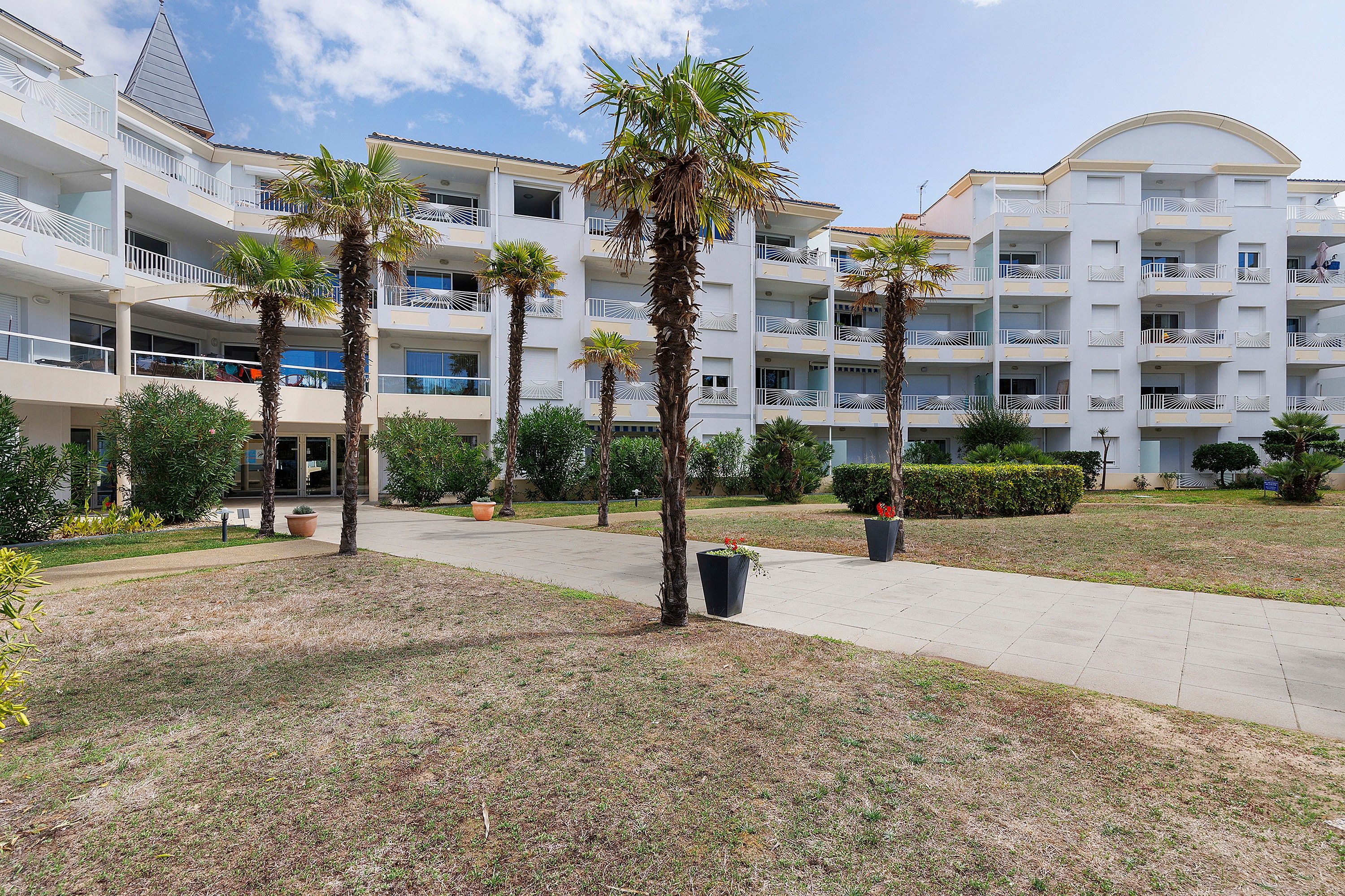 A multi-story hotel with balconies, palm trees, and a paved walkway.