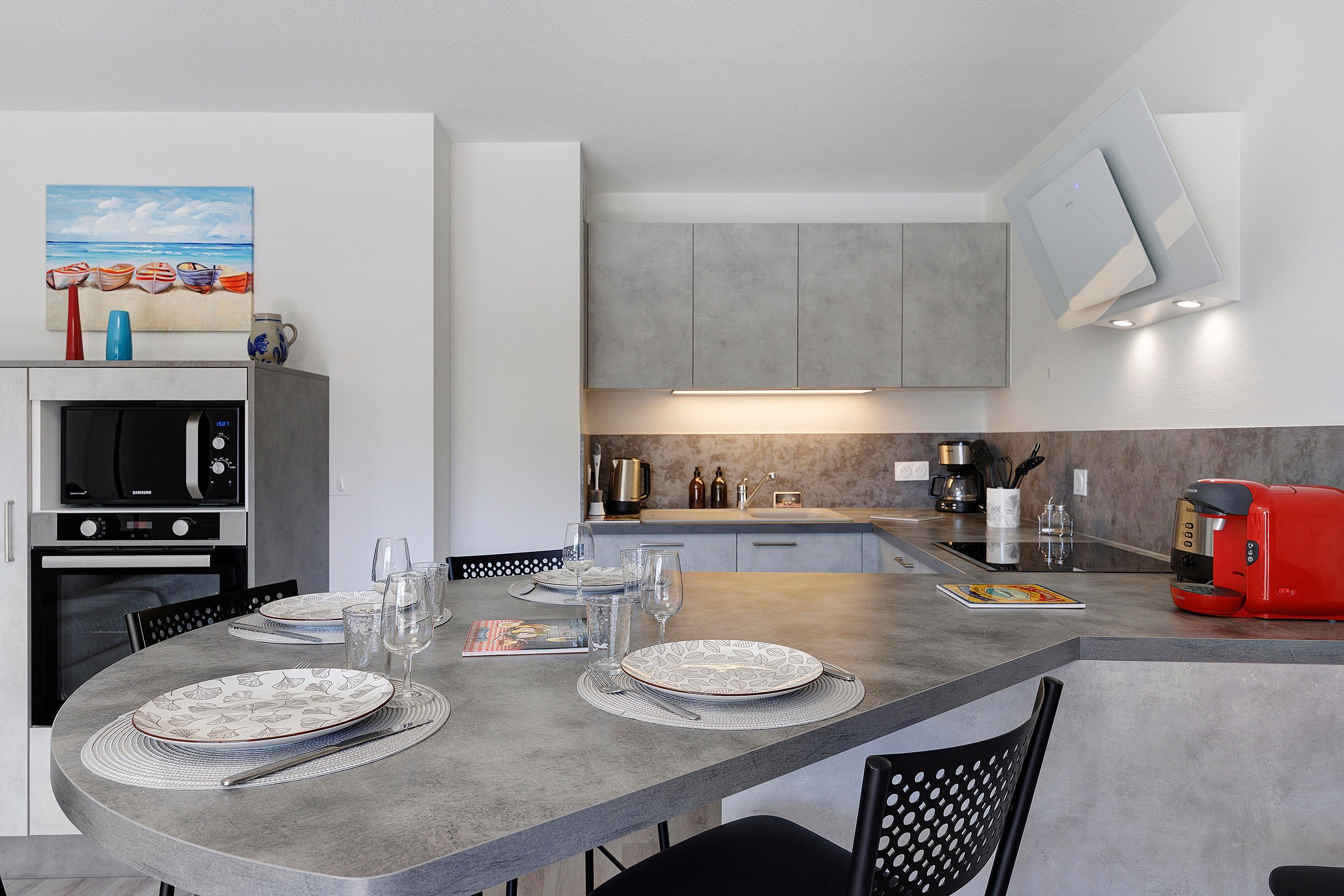 Een moderne keuken met een eethoek, voorzien van een magnetron, oven en een rode koffiezetapparaat.