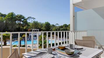 Un balcon avec une table dressée pour le dîner, donnant sur une piscine et des arbres.