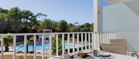 A balcony with a table set for dining, overlooking a swimming pool and trees.