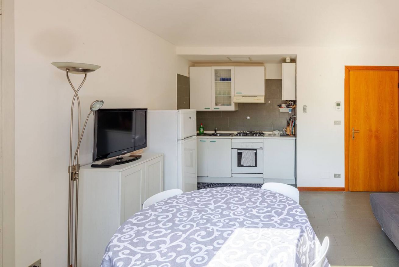 A compact room with a bed, a television, a kitchenette, and a door.