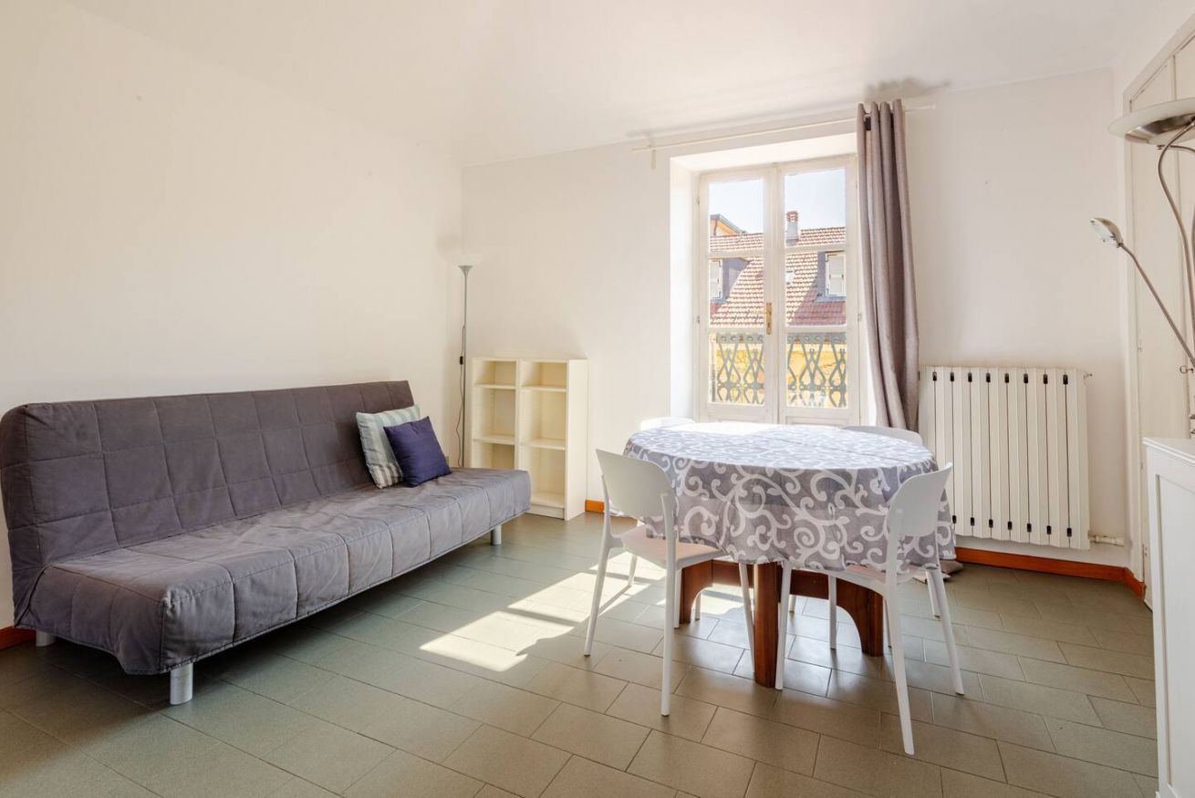 Ein Wohnzimmer mit einer Couch, einem Esstisch mit Stühlen, einer Heizung und einem Fenster mit Vorhängen.