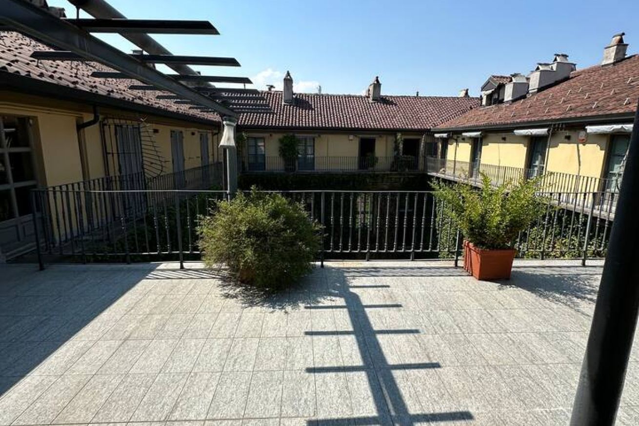 A courtyard with tiled flooring, a metal fence, and potted plants.