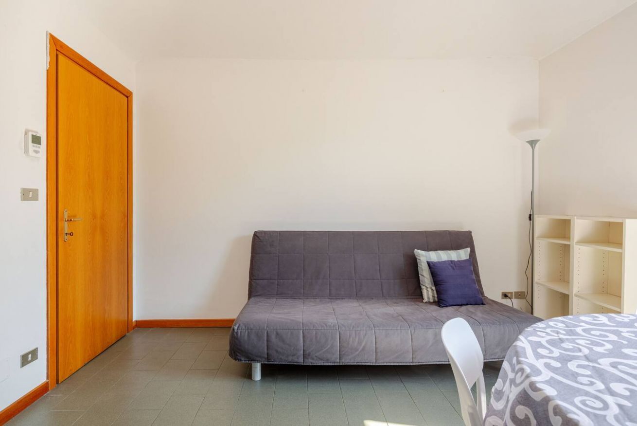 Une pièce avec un canapé gris, une porte en bois, une chaise blanche et un lampadaire.