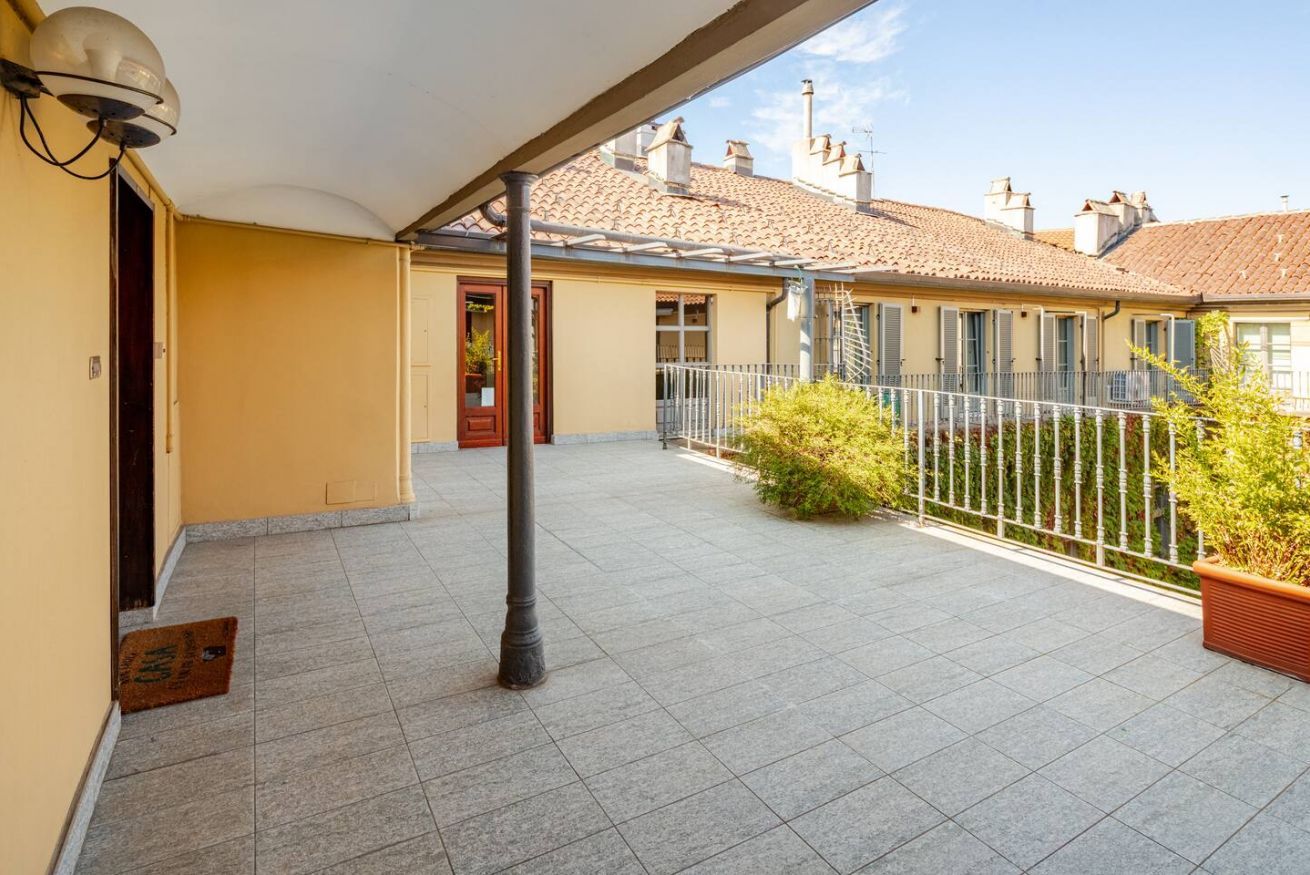 A covered outdoor area with a tiled floor, a metal railing, and a door leading to a building.