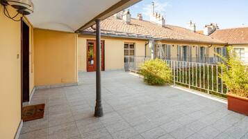 A covered outdoor area with a tiled floor, a metal railing, and a door leading to a building.