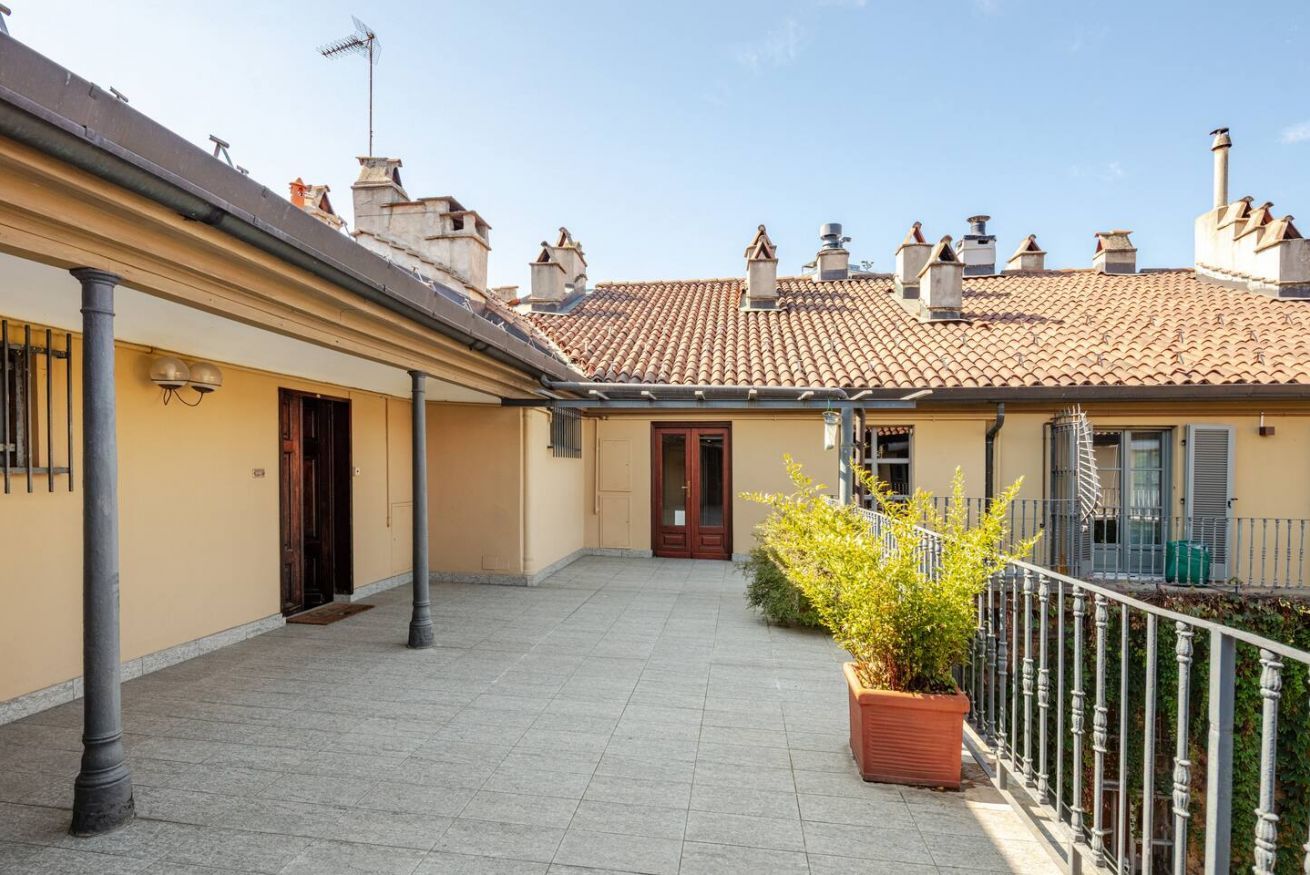 A courtyard with a tiled floor, a potted plant, and a building with a tiled roof and chimneys.