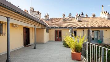 A courtyard with a tiled floor, a potted plant, and a building with a tiled roof and chimneys.