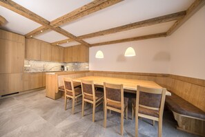 A kitchen with wooden cabinets, a granite countertop, and a dining area with a wooden table and chairs. - Apartment with sauna near ski resort (Hollersbach)