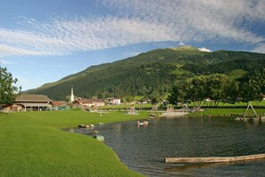 A lakeside park with a grassy area, a small pond, and a church in the background. - Apartment with sauna near ski resort (Hollersbach)
