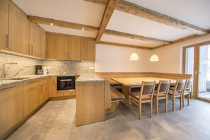 A kitchen with wooden cabinets, a built-in oven, and a dining area with a table and chairs. - Apartment with sauna near ski resort (Hollersbach)