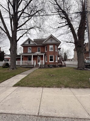 A two-story brick house with a front porch and a small front yard.