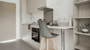 A modern kitchen with a grey chair, a white countertop, and a built-in oven. - Student Only Timber Yard (Bristol)