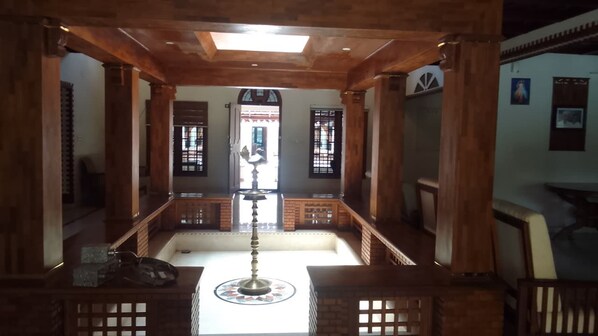 A traditional interior with wooden pillars, a central fountain, and a view of the outside through a window.