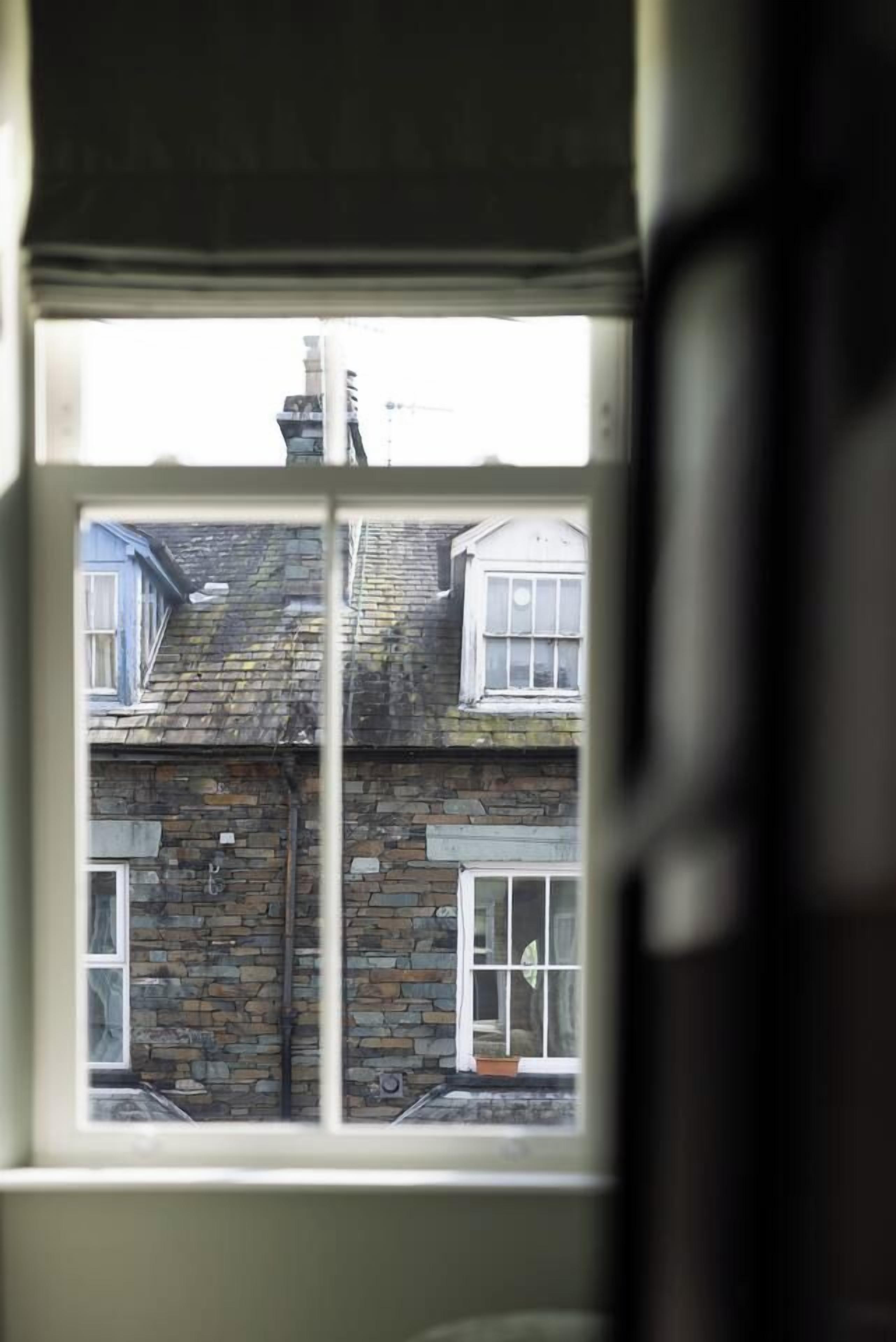 A window with a view of a stone building with multiple windows and a chimney.