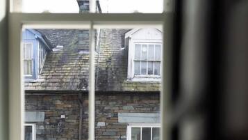 A window with a view of a stone building with multiple windows and a chimney.