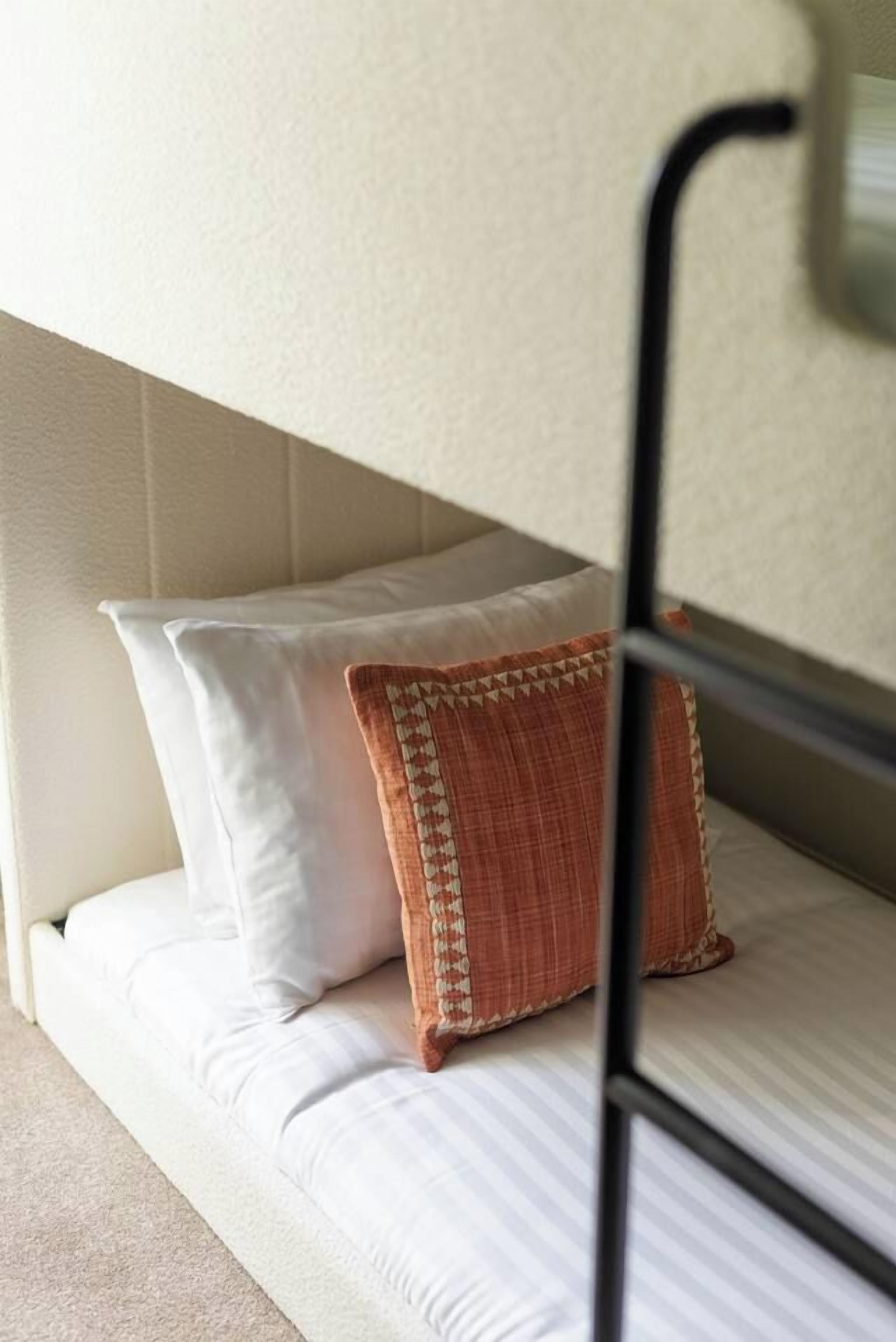 A bunk bed with white bedding and a patterned pillow.