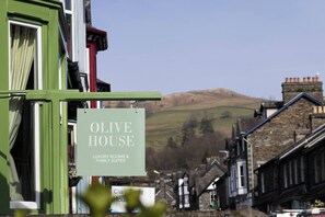 A sign for 'OLIVE HOUSE' with a view of a hill in the background.