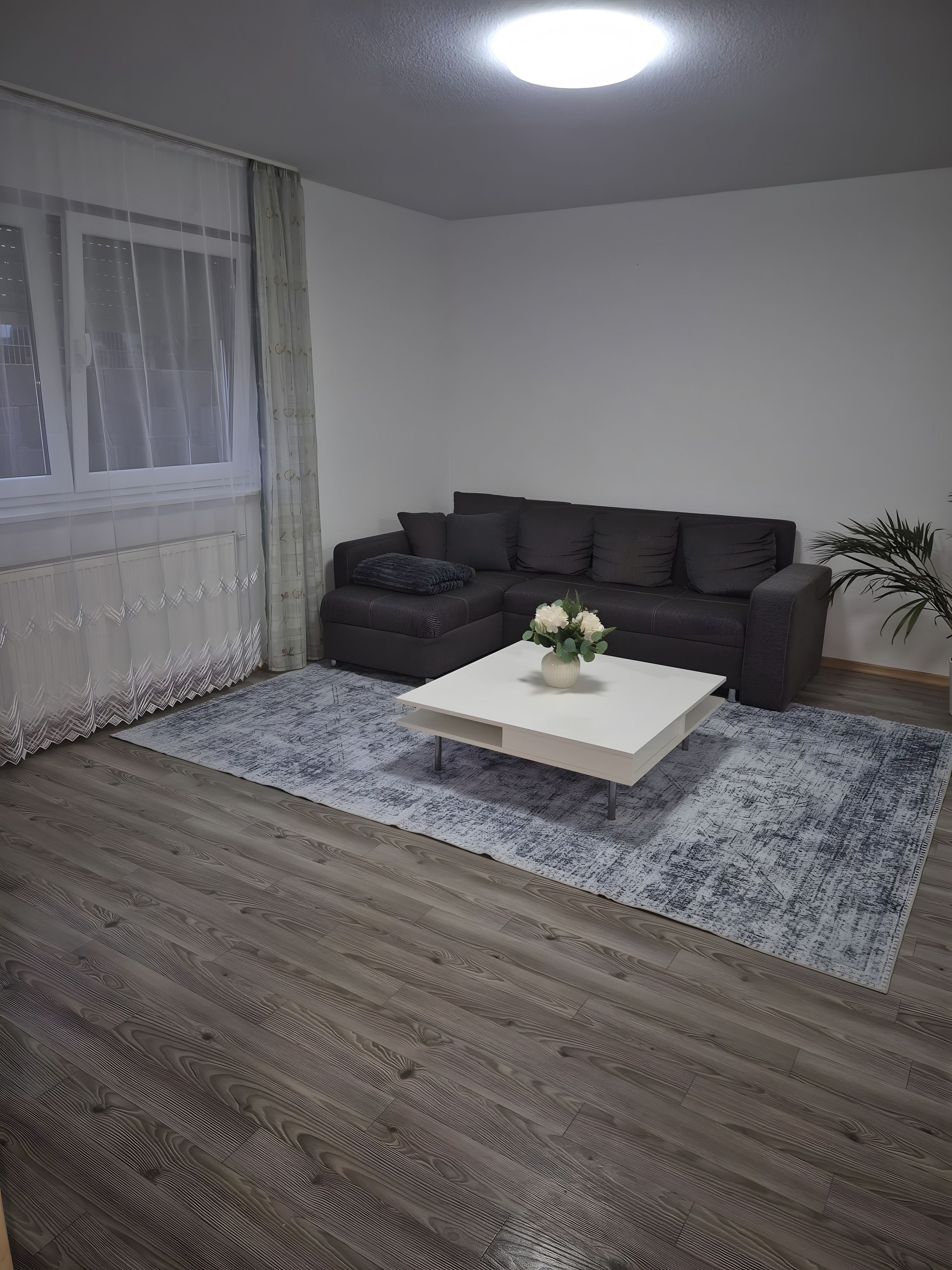 A living room with a dark grey sofa, a white coffee table with a vase of flowers, and a patterned rug.