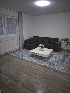 A living room with a dark grey sofa, a white coffee table with a vase of flowers, and a patterned rug. - Apartment 'Fewo Kern' with Wi-Fi (Viernheim)