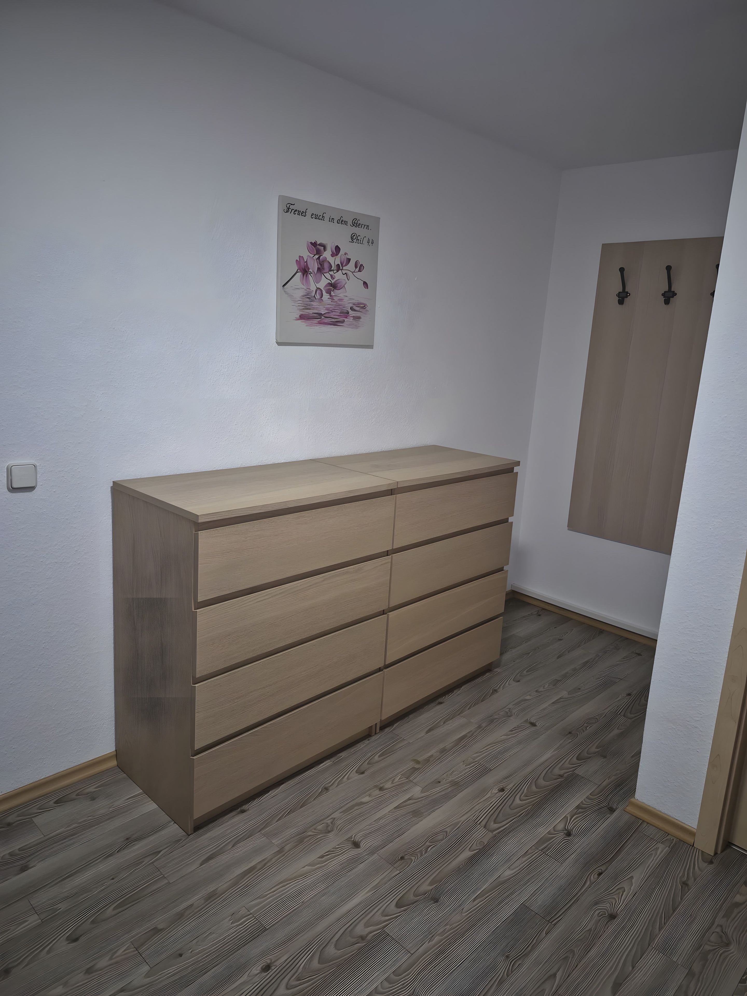 A room with a wooden dresser, a wall-mounted light fixture, and a wooden wardrobe.