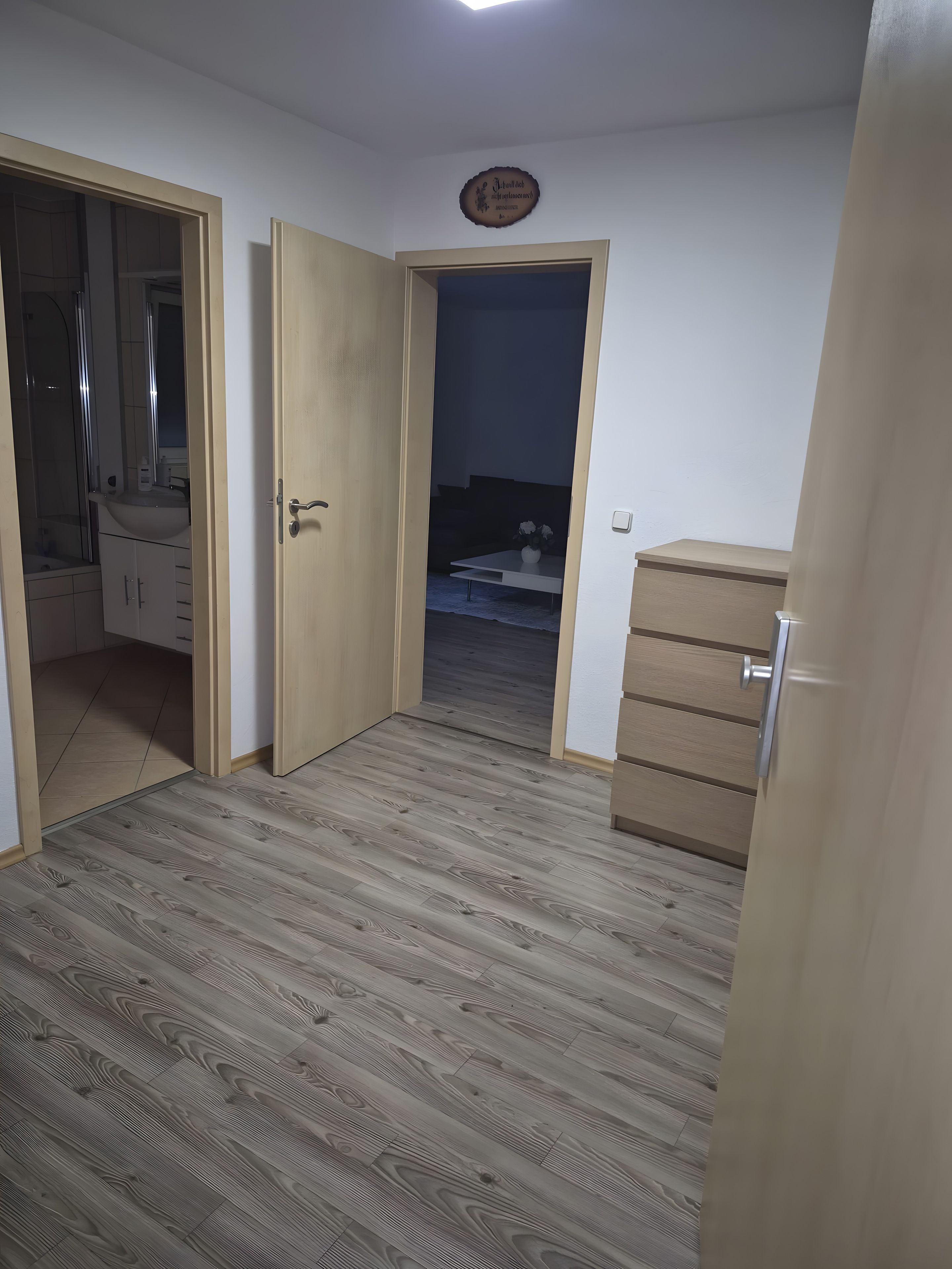 Ein Zimmer mit Holzboden, einer Tür zu einem Badezimmer und einem kleinen Tisch mit einer Vase.