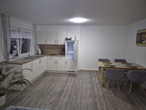 Een compacte keuken met witte kastjes, een inbouwoven en een eethoek met een houten tafel en stoelen.