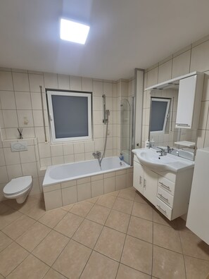 A modern bathroom with a bathtub, a toilet, and a sink with a mirror. - Apartment 'Fewo Kern' with Wi-Fi (Viernheim)