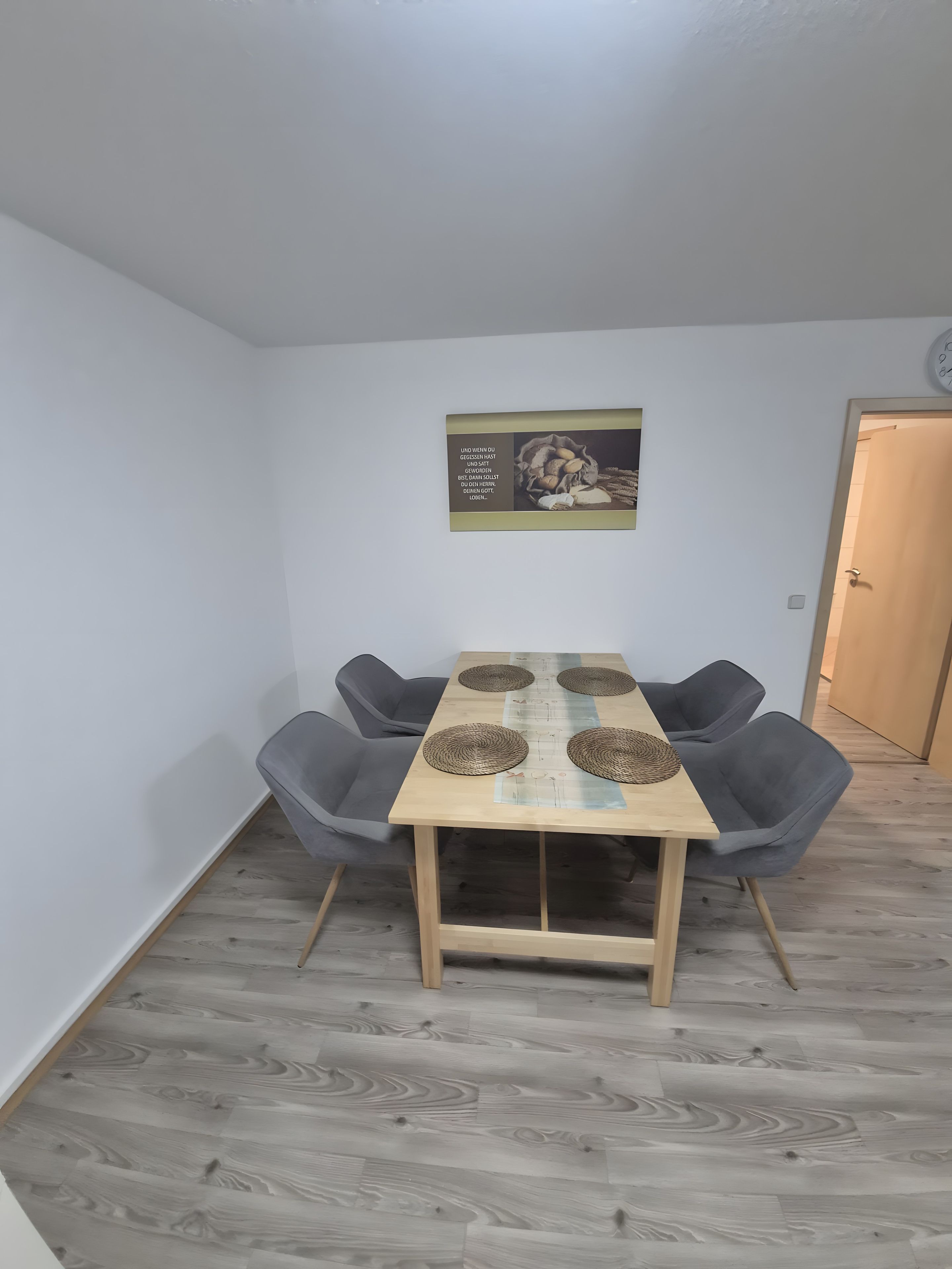 A dining area with a wooden table, four grey chairs, and a wall-mounted picture.