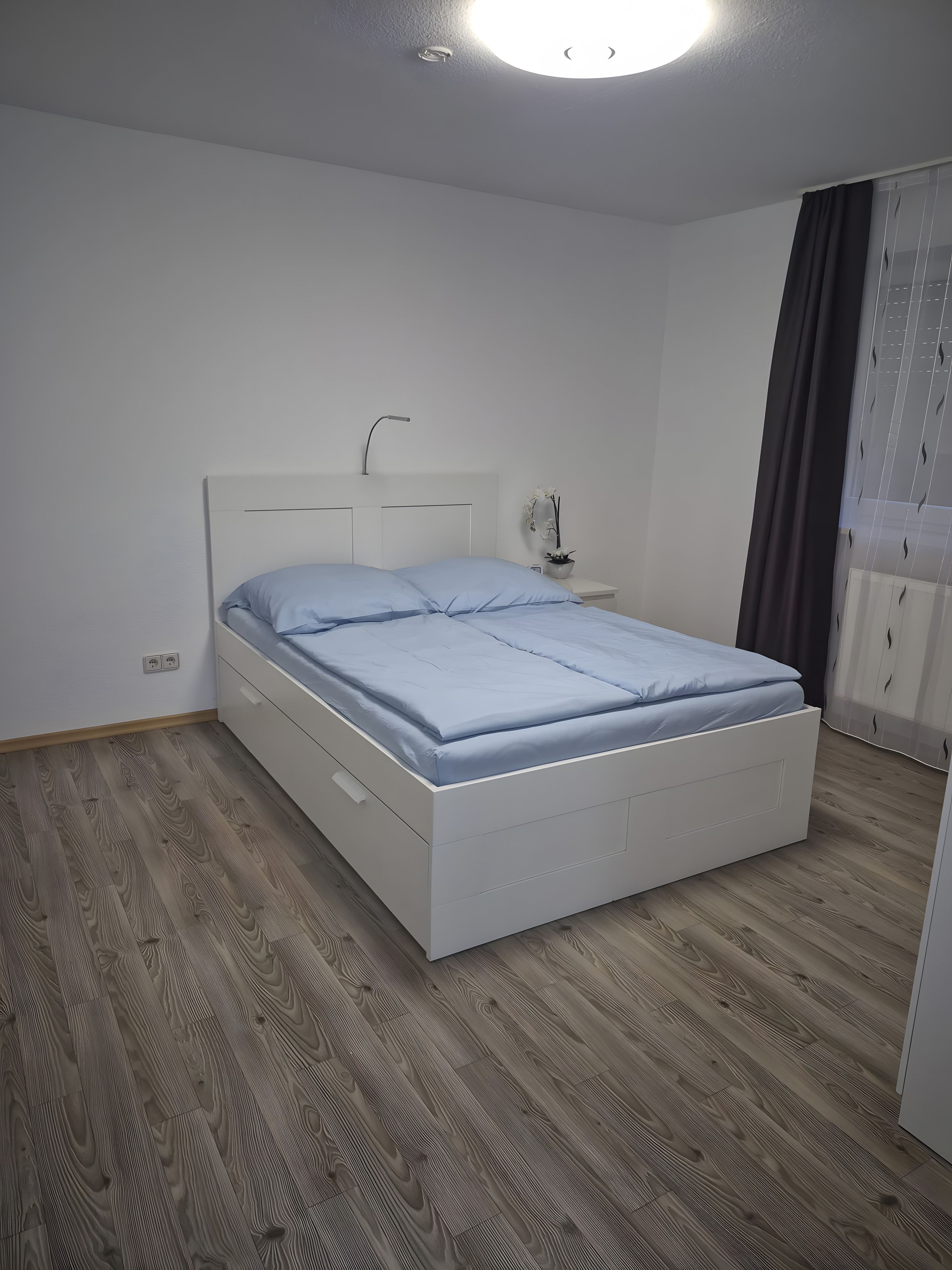 A bedroom with a single bed, a bedside table, a nightstand, and a window with curtains.
