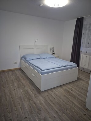 Een slaapkamer met een enkel bed, een nachtkastje en een raam met gordijnen.