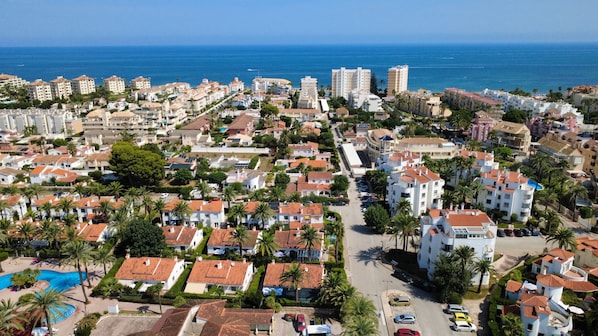 Zona residencial costanera amb diversos edificis, incloent habitatges i cases d'apartaments amb teulades vermelles, envoltada de palmeres i amb una vista despejada del mar.