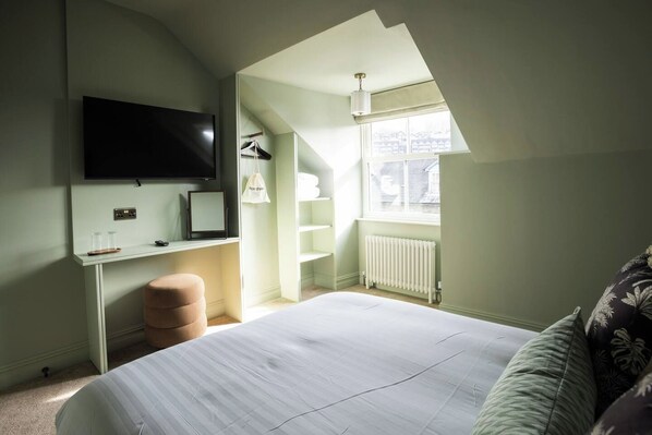 Une chambre avec un lit, un bureau, un téléviseur fixé au mur, un radiateur et une fenêtre donnant sur un beau paysage.
