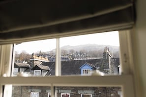 A view through a window of a residential area with houses, a stone structure, and a hill in the background.