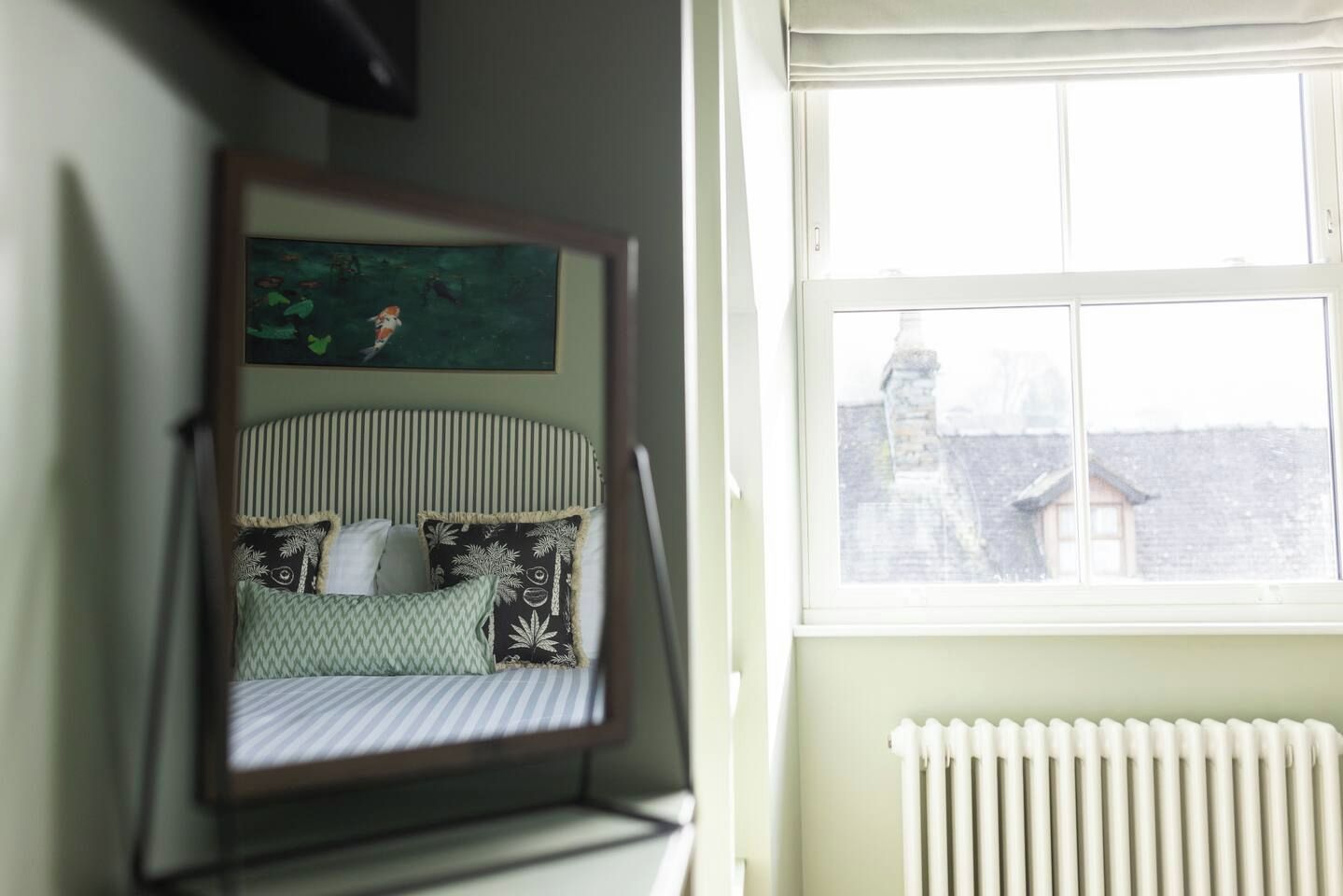 A room with a crib, a radiator, and a window with a view of a building.