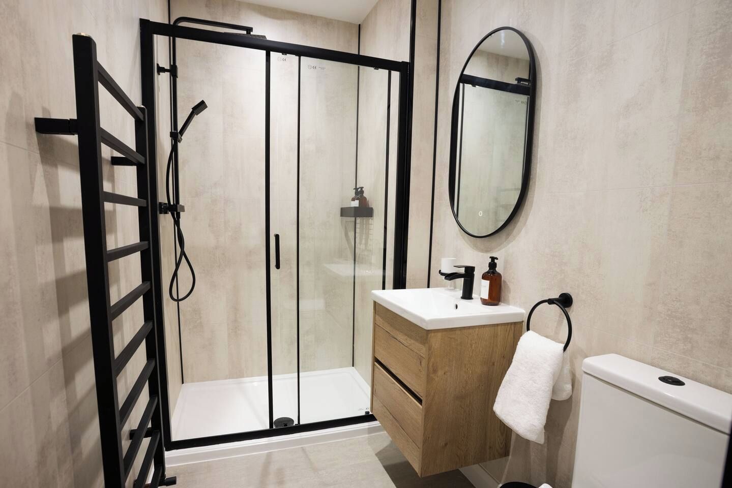 A modern bathroom with a glass shower enclosure, a wooden vanity, a white toilet, and a round mirror.