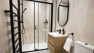 A modern bathroom with a glass shower enclosure, a wooden vanity, a white toilet, and a round mirror.