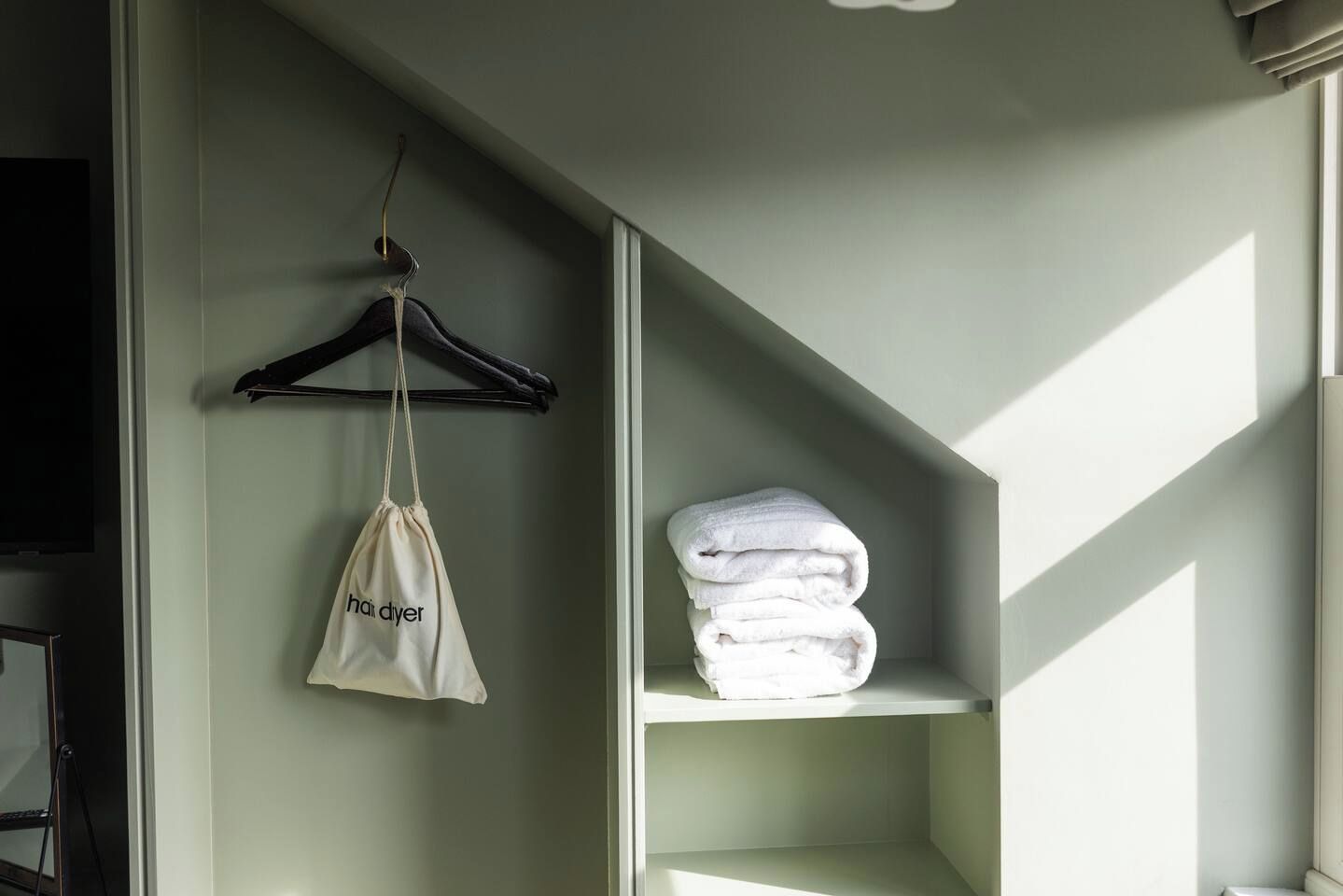 A room with a hanging garment bag and a stack of folded towels on a shelf.