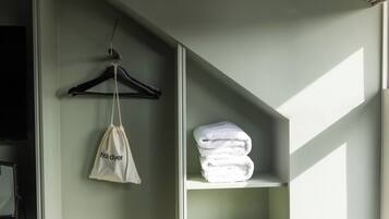 A room with a hanging garment bag and a stack of folded towels on a shelf.