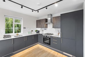 A modern kitchen with dark cabinets, a gas stove, and a window with a view of greenery. - 2bedroom 2bathroom Penthouse Wembley Stadium (Wembley)