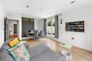 Ein modernes Wohnzimmer mit einem grauen Sofa, einem kleinen runden Tisch und einem Essbereich mit Stühlen.