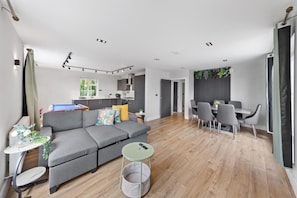 A modern living room with a grey sofa, a dining area with grey chairs, a kitchen with dark cabinets, and a pool table. - 2bedroom 2bathroom Penthouse Wembley Stadium (Wembley)