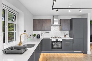 A modern kitchen with a large window, a gas stove, and dark cabinetry. - 2bedroom 2bathroom Penthouse Wembley Stadium (Wembley)