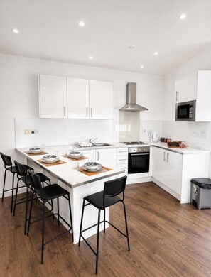 Une cuisine moderne avec des meubles blancs, un îlot central doté de tabourets, une hotte en acier inoxydable et un four à micro-ondes placé au-dessus du four traditionnel.