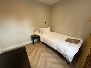 A bedroom with a bed, a nightstand, a lamp, and a wooden floor. - 5 Bed Home - Contractors & Professionals - Wifi (Luton)