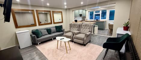 A modern living room with a sofa, armchairs, a coffee table, and a dining area with a table and chairs.