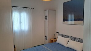 Een slaapkamer met een bed, een kledingkast, een nachtkastje en een schilderij aan de muur.