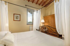 Quarto com cama, cortinas, janela, radiador, armário de madeira e um quadro na parede.